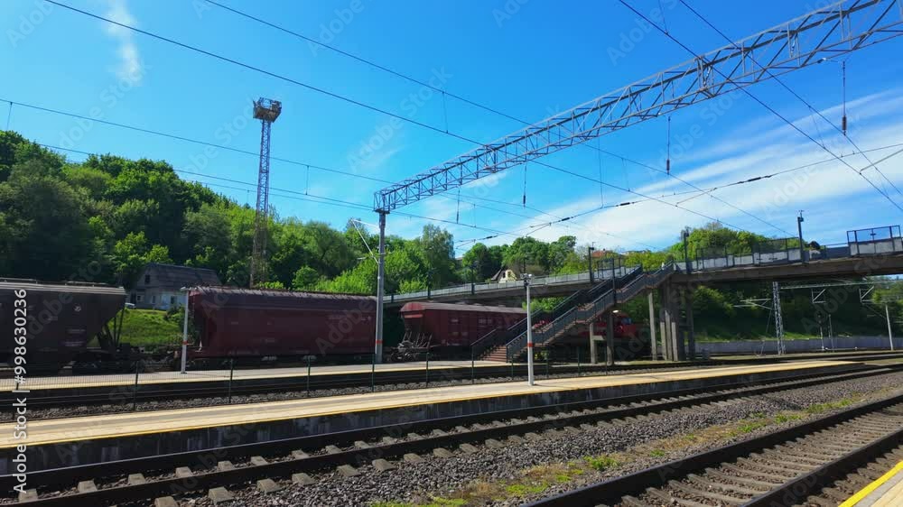 A quiet train station with empty platforms and rail tracks on a sunny day, featuring a bridge, power lines, and green trees in the background. Ideal for transportation, travel, and railway themes. A quiet train station with empty platforms and rail tracks on a sunny day, featuring a bridge, power lines, and green trees in the background. Ideal for transportation, travel, and railway themes.