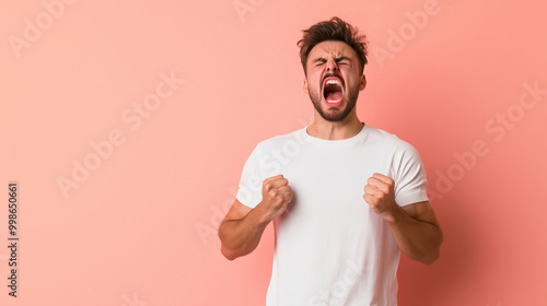 A man gritting his teeth, fists clenched at his sides, showing frustration and anger, standing against a light pastel peach background. photo