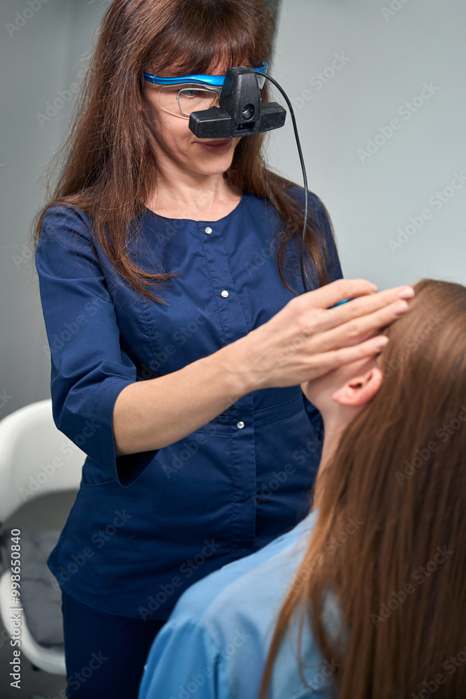 Fototapeta premium Optometrist inspecting patients head with hands during eye exam