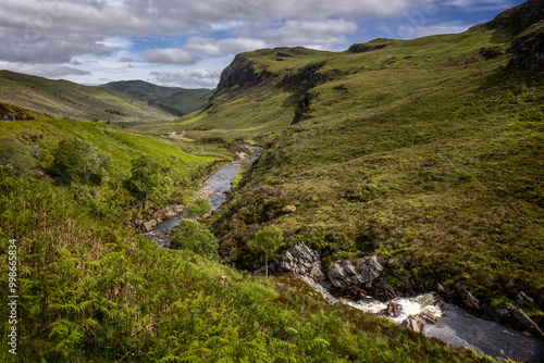 Typical Scottish landscape with hills, rocks, a cloudy blue sky and the many rivers and lochs in the Scottish highlands.