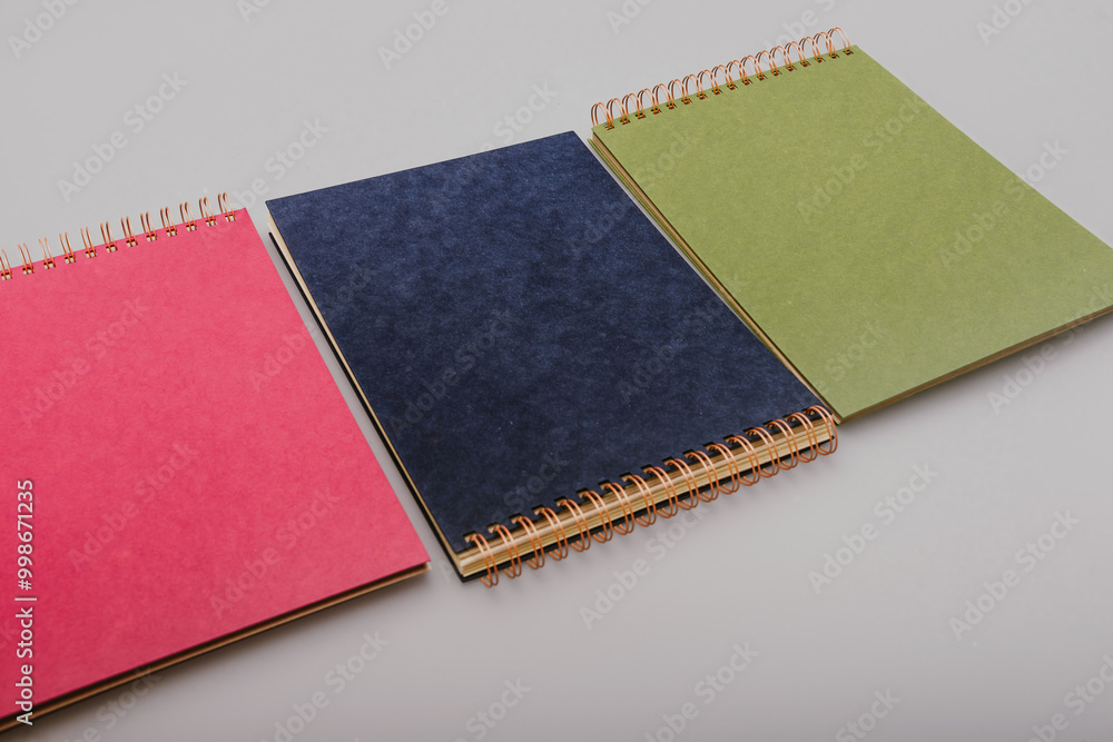 Fototapeta premium Stack of three colourful craft paper spiral binding photo albums in blue, green, and magenta. Ideal for DIY scrapbooking, memory keeping, and creative photo displays in vibrant styles.