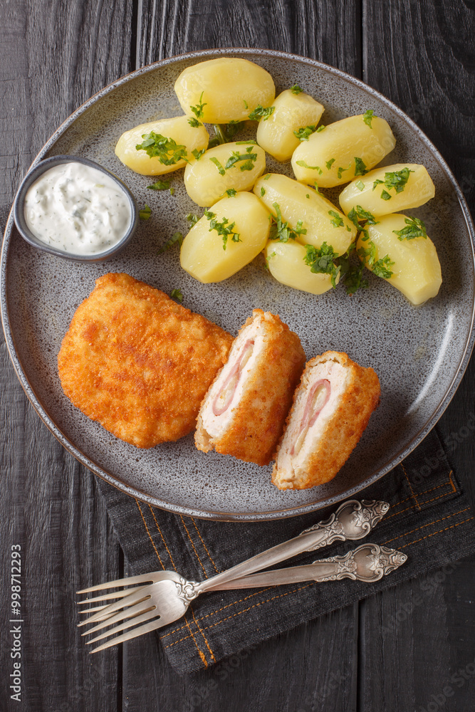 Classic cordon bleu with new potatoes and cream sauce close-up on a plate on a table. Vertical top view from above
