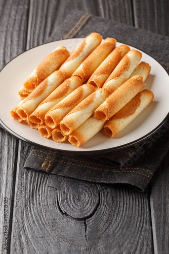 Russian cigarettes are thin, delicate wafers rolled into a roll and baked until golden brown and crispy, close-up on a plate on the table. Vertical