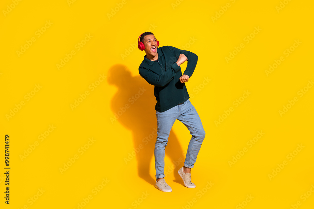 Full length photo of attractive young man headphones dancing dressed stylish green clothes isolated on yellow color background Full length photo of attractive young man headphones dancing dressed stylish green clothes isolated on yellow color background