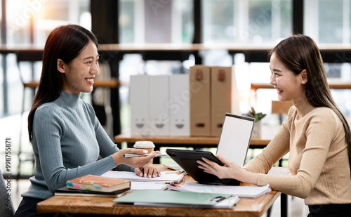 Two asian lady colleagues discussing new project, businesswomen using digital tablet together in office