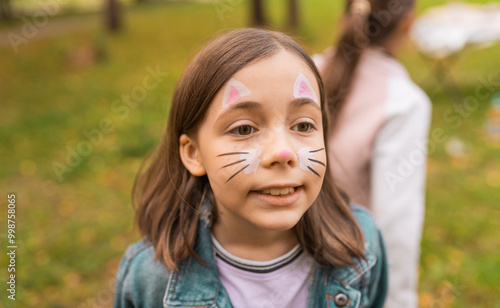 Portrait of a cute little girl with face painting of a cat outdoors. Child having fun at a party outside.