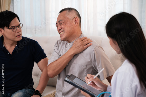 Asian female doctor examines an elderly patient with neck pain at home.