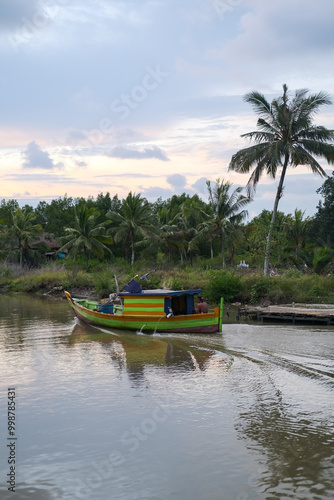 Obraz na płótnie Colorful fishing boats docked along the concrete pier at Pelabuhan Kuala Singkawang, Kalimantan Barat, with village buildings and lush trees in the background, capturing coastal life. w salonie