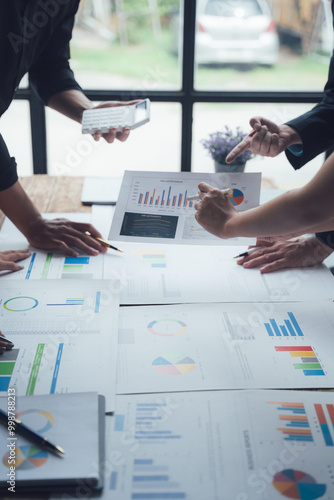 Strategic Business Meeting: Hands-on collaboration around a table strewn with financial reports and data analysis charts.  A close-up shot emphasizing teamwork and focused problem-solving.