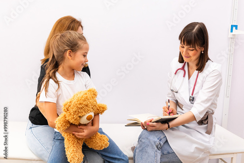 Mom bring her child, little daughter to the pediatrician office, register her and discuss with the doctor how to care for the children. Healthy lifestyle. The doctor fills out the health questionnaire photo