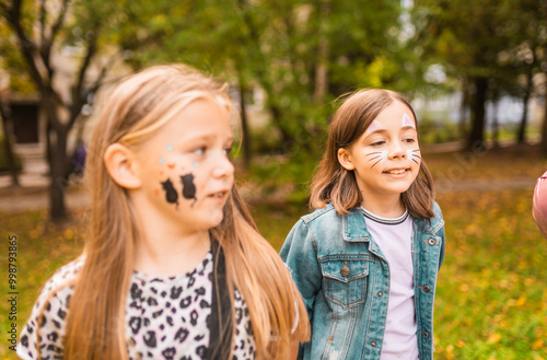 Portrait of a cute little girls with face painting of a cat outdoors. Child having fun at a party outside.