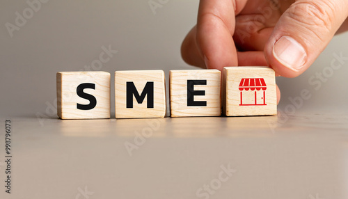 SME Concept with Wooden Cubes Representing Small and Medium Enterprises, Hand Arranging Blocks with Shop Icon, Symbolizing Retail and Local Business Development.