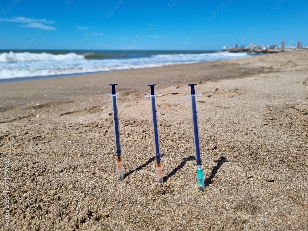 Three syringes on a sandy beach with ocean in the background Three syringes on a sandy beach with ocean in the background