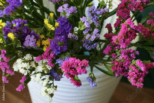 Bouquet of multicolored flowers in a vase (Limonium sinuatum, Statice sinuata) on a green background photo