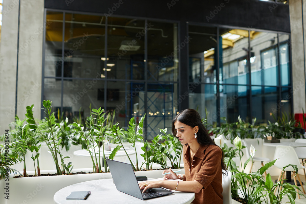Successful woman typing on laptop planning business strategy while working at cafe table in contemporary office building, copy space Successful woman typing on laptop planning business strategy while working at cafe table in contemporary office building, copy space