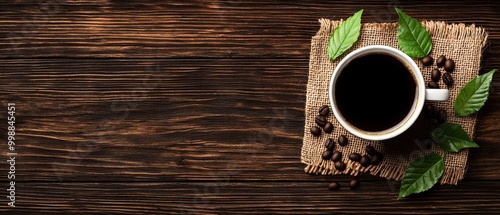  A cup of coffee atop a burlwood table, beside coffee beans and a verdant leaf photo