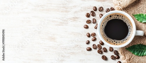  A cup of coffee atop a table, nearby sits a stack of coffee beans and a verdant leaf