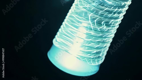 closeup flickering fluorescent lamp gently illuminating dark space swaying electric wire 4K footage highlights energy efficient spiral tube bulb being switched showcasing interplay