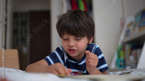 Young boy intently focusing on a small toy or puzzle while sitting on his bed in a child’s room, demonstrating concentration and engagement