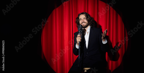 Caucasian man comic in costume performing standup monologue on stage with red curtains. Concept comedian show banner photo