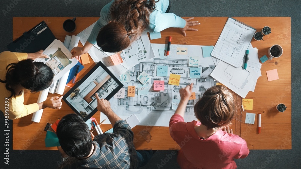 Top view of engineer working together to design building construction while standing at meeting table with blueprint and notes. Top view of interior designer choosing color from palettes. Symposium. Top view of engineer working together to design building construction while standing at meeting table with blueprint and notes. Top view of interior designer choosing color from palettes. Symposium.
