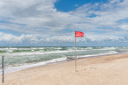 a red flag flying in a wind on a sunny windy day at a beach