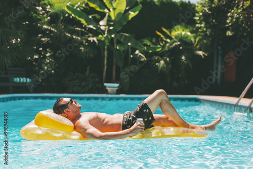 A man laying on a floatie in a backyard pool in summer.  photo