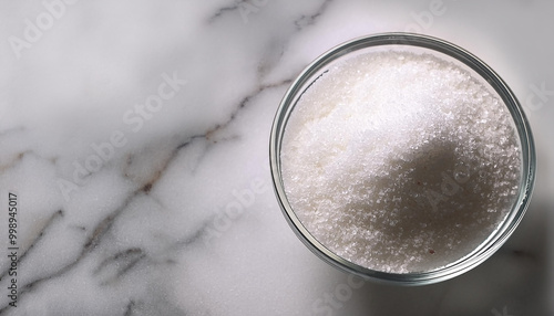 Granulated sugar in a glass bowl on a marble background