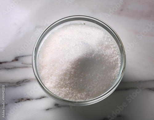Granulated sugar in a glass bowl on a marble background