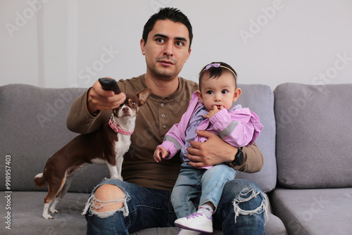 Young dad with baby in arms grabs tv remote control