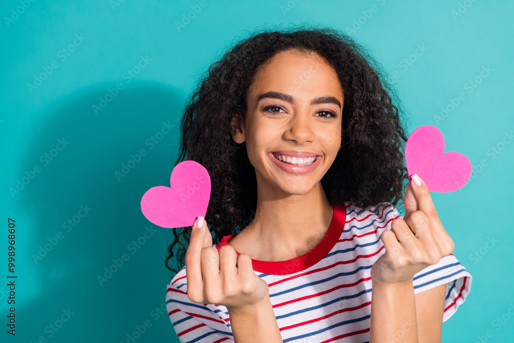 Photo portrait of pretty young girl hold pink heart postcards wear trendy striped outfit isolated on cyan color background Photo portrait of pretty young girl hold pink heart postcards wear trendy striped outfit isolated on cyan color background