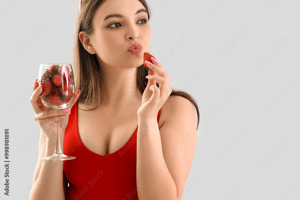 Φωτογραφία Young woman in swimsuit with glass of strawberries on light background, closeup