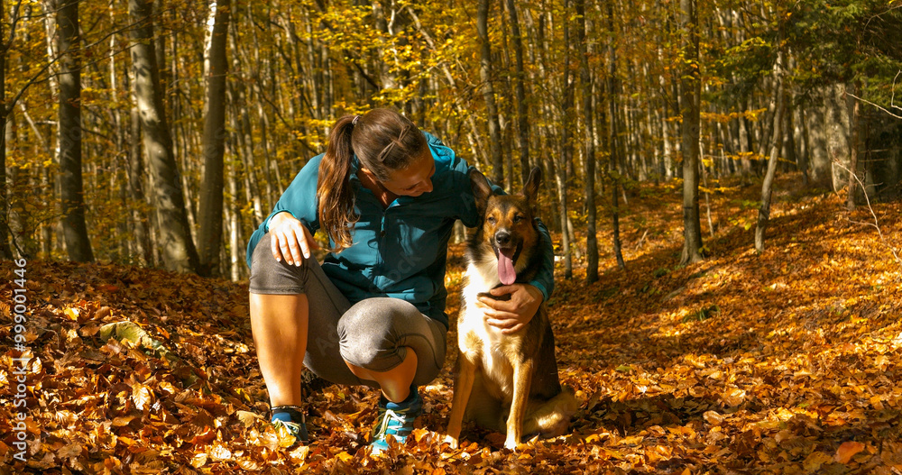CLOSE UP, PORTRAIT: Smiling pet owner hugs her cute mixed breed dog while walking in colorful autumn forest. Lady and her doggo enjoying outdoor adventures on a beautiful sunny day in fall season. CLOSE UP, PORTRAIT: Smiling pet owner hugs her cute mixed breed dog while walking in colorful autumn forest. Lady and her doggo enjoying outdoor adventures on a beautiful sunny day in fall season.