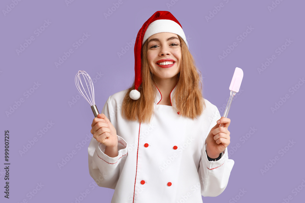 Young female chef in Santa hat with whisk and spatula on purple background