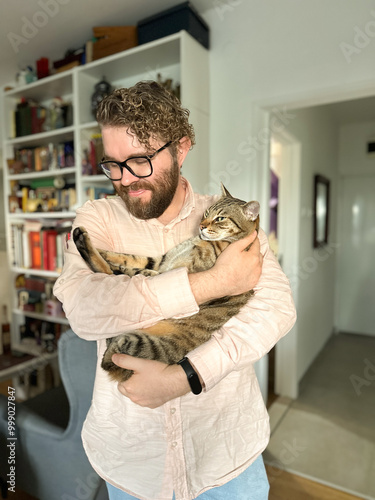 Handsome millennial man holds a tabby cat in his arms and kisses it. Pet and friendship concept
