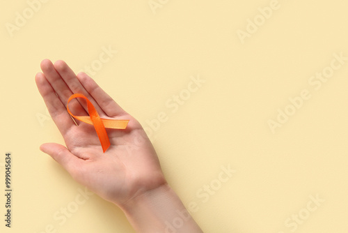 Female hand with orange ribbon on yellow background. World Cancer Day photo