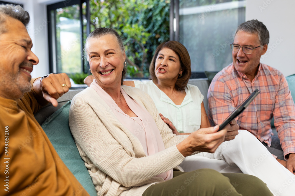 Senior diverse friends sitting on couch, smiling and holding tablet, enjoying conversation, at home Senior diverse friends sitting on couch, smiling and holding tablet, enjoying conversation, at home