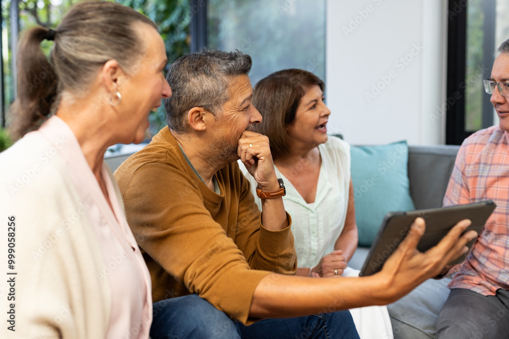 Laughing together, senior diverse friends using tablet and enjoying conversation on couch, at home Laughing together, senior diverse friends using tablet and enjoying conversation on couch, at home