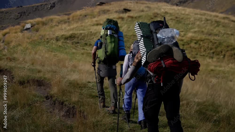 Three hikers climbing a grassy hill in slow motion showcase outdoor adventure and camaraderie, equipped with backpacks and trekking poles under a bright, sunny sky Three hikers climbing a grassy hill in slow motion showcase outdoor adventure and camaraderie, equipped with backpacks and trekking poles under a bright, sunny sky