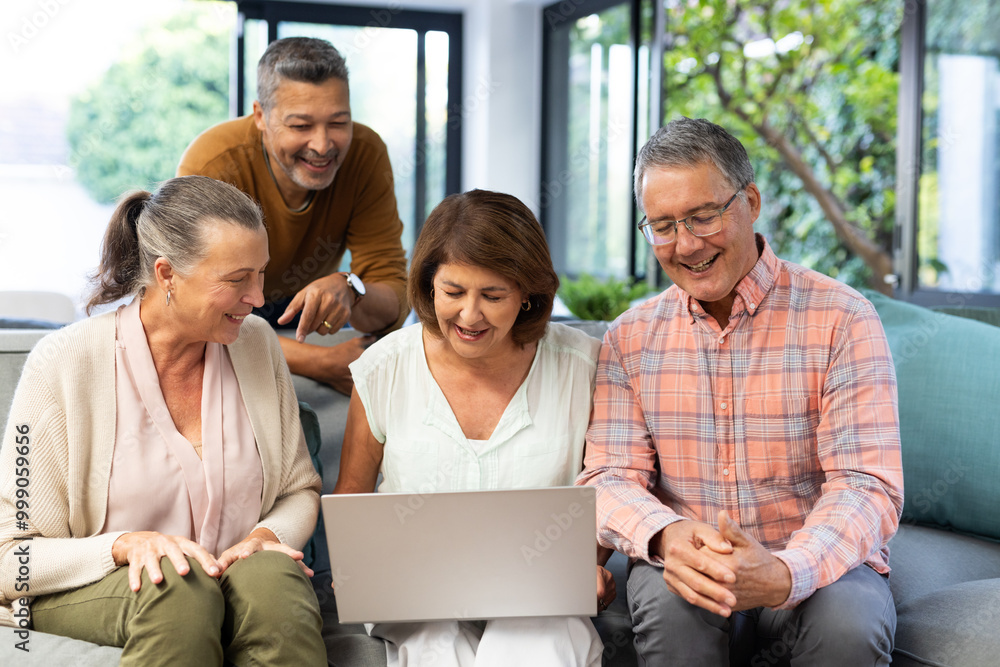 Group of senior diverse friends sitting on couch, smiling and looking at laptop, at home Group of senior diverse friends sitting on couch, smiling and looking at laptop, at home