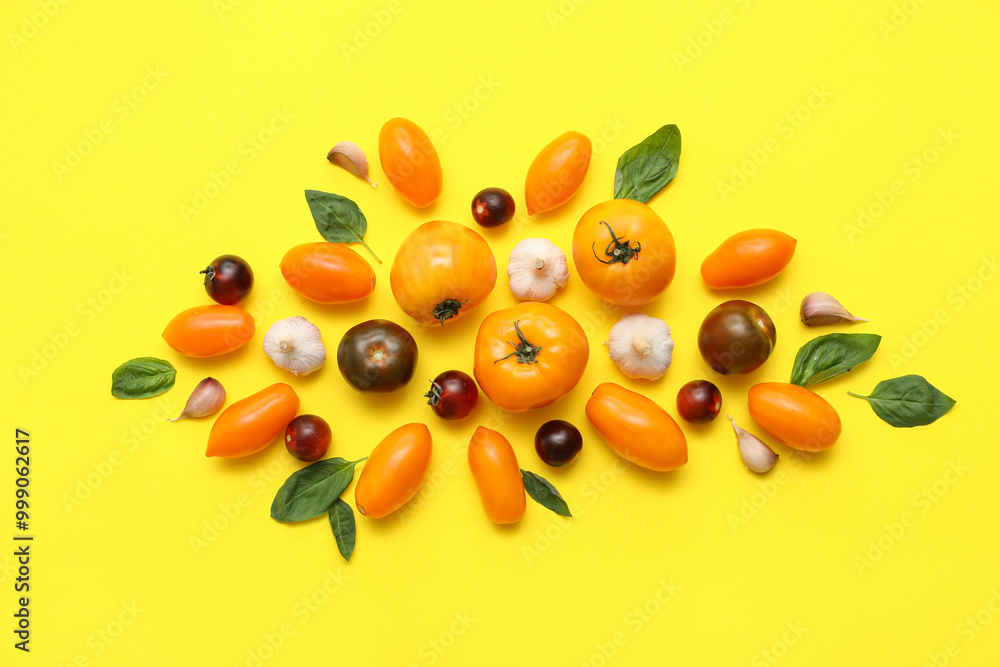Different fresh tomatoes with garlic and basil on yellow background Different fresh tomatoes with garlic and basil on yellow background