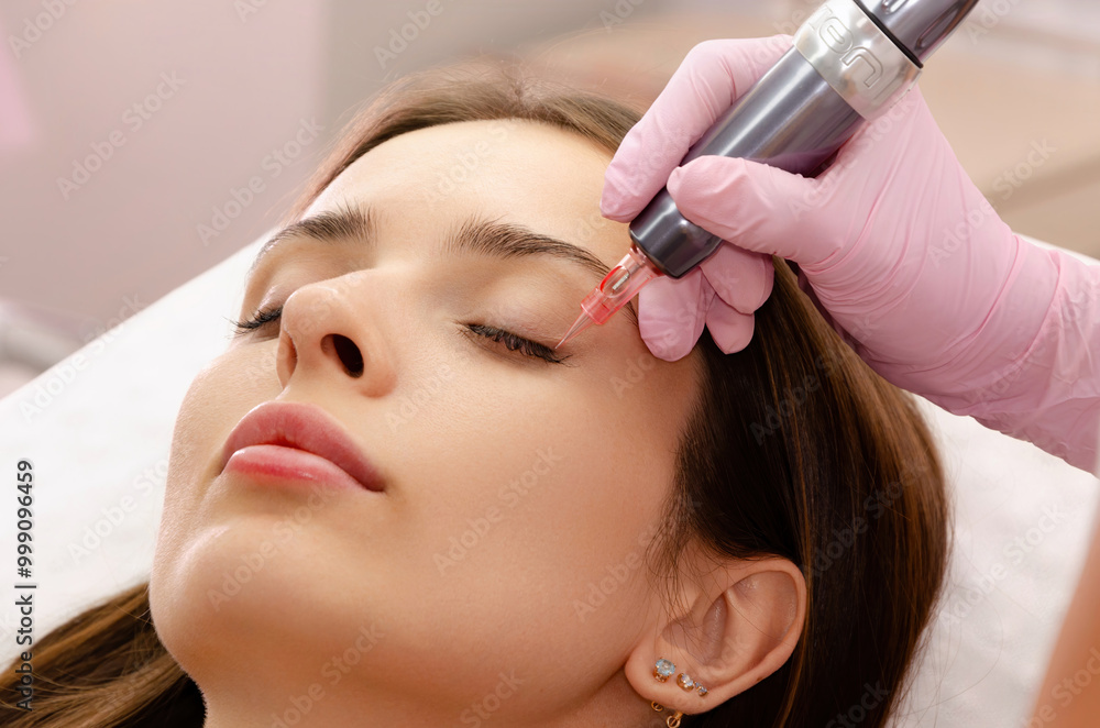 Fototapeta premium Young woman getting eyeliner tattoo procedure in beauty salon. Beauty and skin care concept.