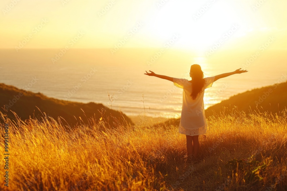Woman with arms outstretched on a grassy hill, basking in the warm golden light of a beautiful sunrise over the ocean, embodying happiness and peace. Woman with arms outstretched on a grassy hill, basking in the warm golden light of a beautiful sunrise over the ocean, embodying happiness and peace.