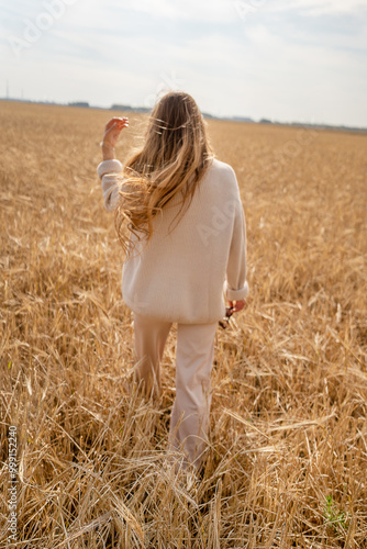 A woman walks through a vibrant wheat field under a sunny blue sky, enjoying natures beauty