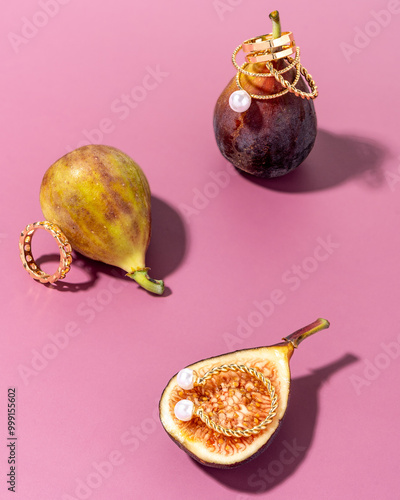 Figs and stacked golden rings with pearls on a purple pink background