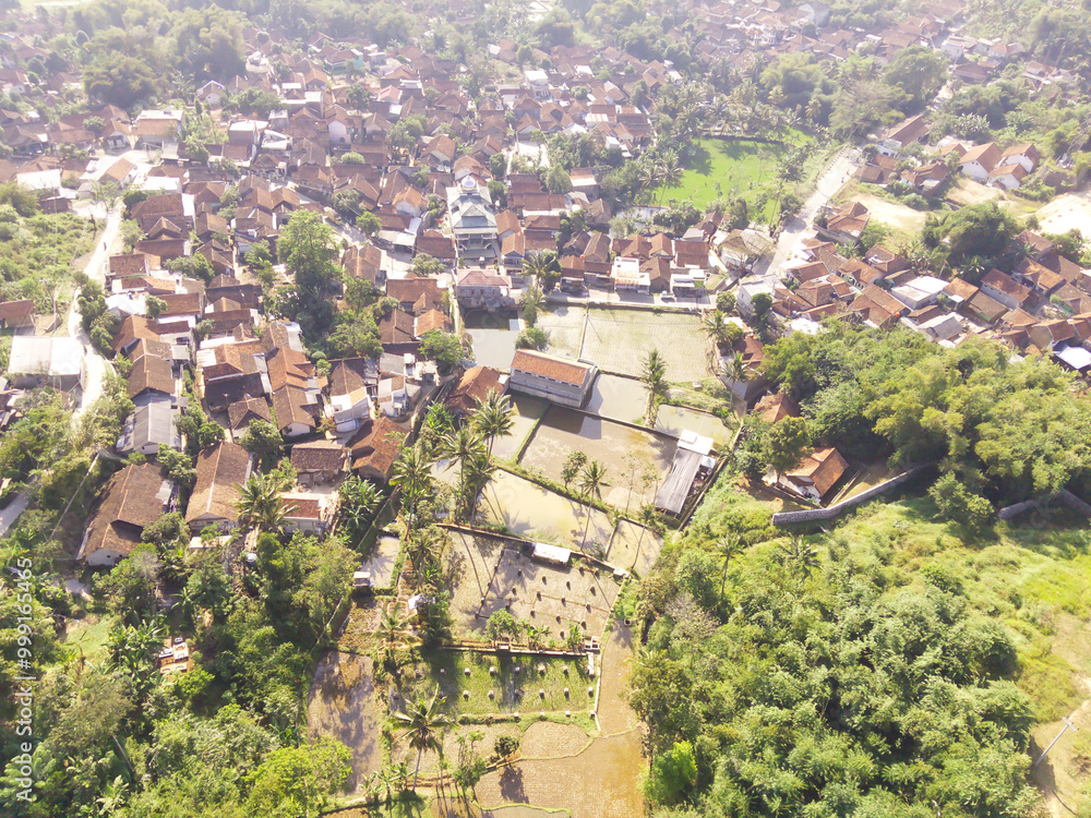 Fototapeta premium Photography of residential district from aerial perspective. A small village surrounded by green rice fields in Bandung Regency - Indonesia. Residential Settlement. Rural Scenery. Aerial Photography