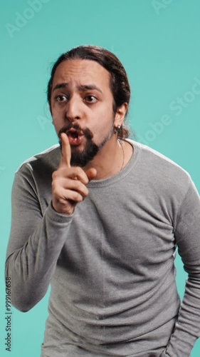 Vertical video Portrait of man doing shushing hand gesturing, requesting silence. Person placing finger on lips, doing quiet sign gesture, asking for secrecy, isolated over studio background, camera B photo