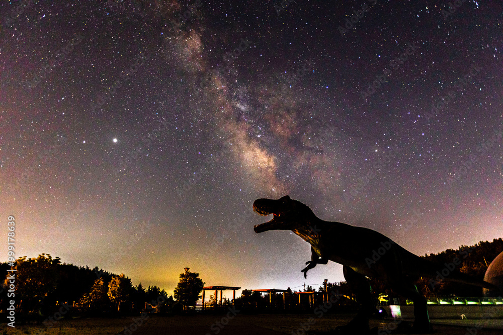 Naklejka premium Bibong Dinosaur Park, Boseong-gun, Jeollanam-do, South Korea - May 23, 2020: Dinosaur sculptures against galaxy of night sky at Dinosaur museum