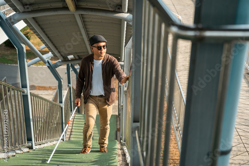 Young blind man walking in city with walking stick. Visually impaired man difficult to traveling on the road wearing sun glasses Cross the road cross the footbridge photo