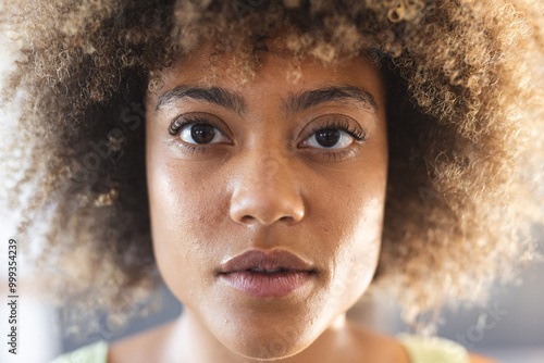 Close-up portrait of woman with curly hair, looking directly at camera, at home